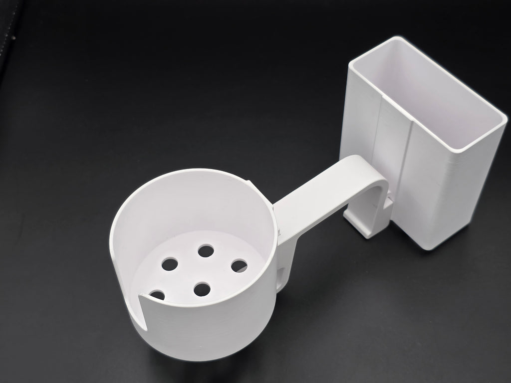 A studio-style shot of a single white, 3D-printed cup and cell phone holder attachment for a Hastings poly stock tank, isolated against a smooth black background. The cup holder features a deep cylindrical cup with five drainage holes at the bottom and a large side notch for mug handles. The cell phone holder is rectangular with rounded corners. Both holders are connected to a sturdy, integrated L-shaped mounting clip designed to hook over a thick tank rim, showcasing the smooth finish.