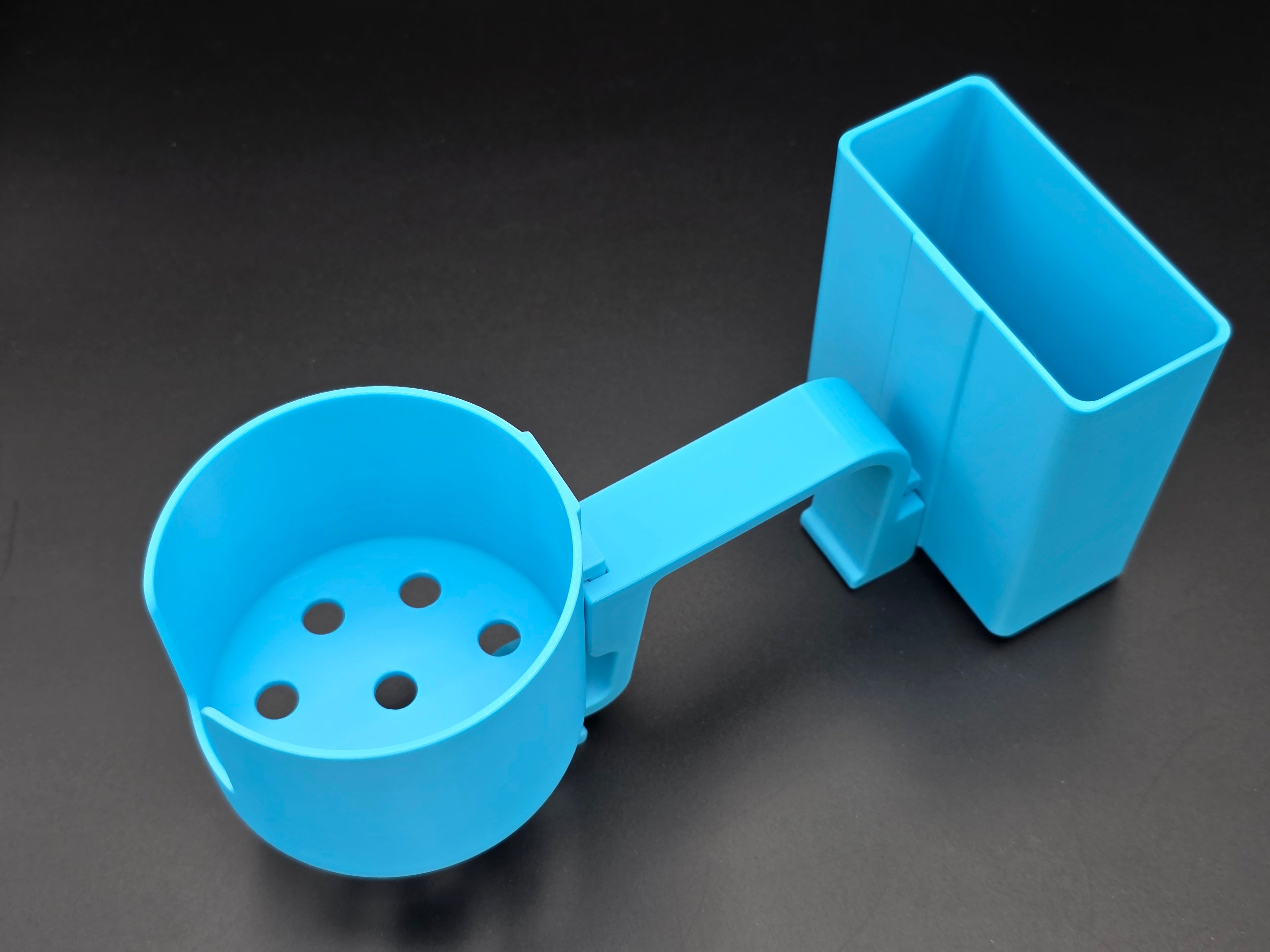 A studio-style shot of a single light blue, 3D-printed cup and cell phone holder attachment for a Hastings poly stock tank, isolated against a smooth black background. The cup holder features a deep cylindrical cup with five drainage holes at the bottom and a large side notch for mug handles. The cell phone holder is rectangular with rounded corners. Both holders are connected to a sturdy, integrated L-shaped mounting clip designed to hook over a thick tank rim, showcasing the smooth finish.
