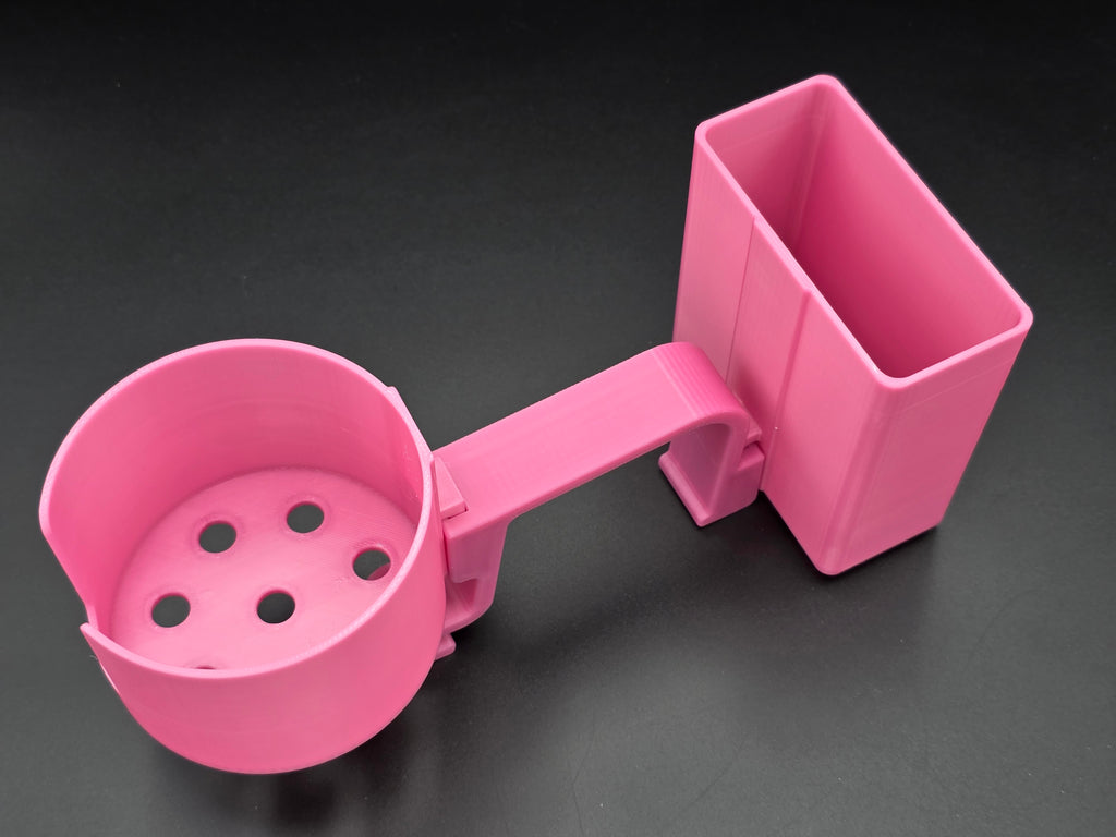 A studio-style shot of a single pink, 3D-printed cup and cell phone holder attachment for a Hastings poly stock tank, isolated against a smooth black background. The cup holder features a deep cylindrical cup with five drainage holes at the bottom and a large side notch for mug handles. The cell phone holder is rectangular with rounded corners. Both holders are connected to a sturdy, integrated L-shaped mounting clip designed to hook over a thick tank rim, showcasing the smooth finish.