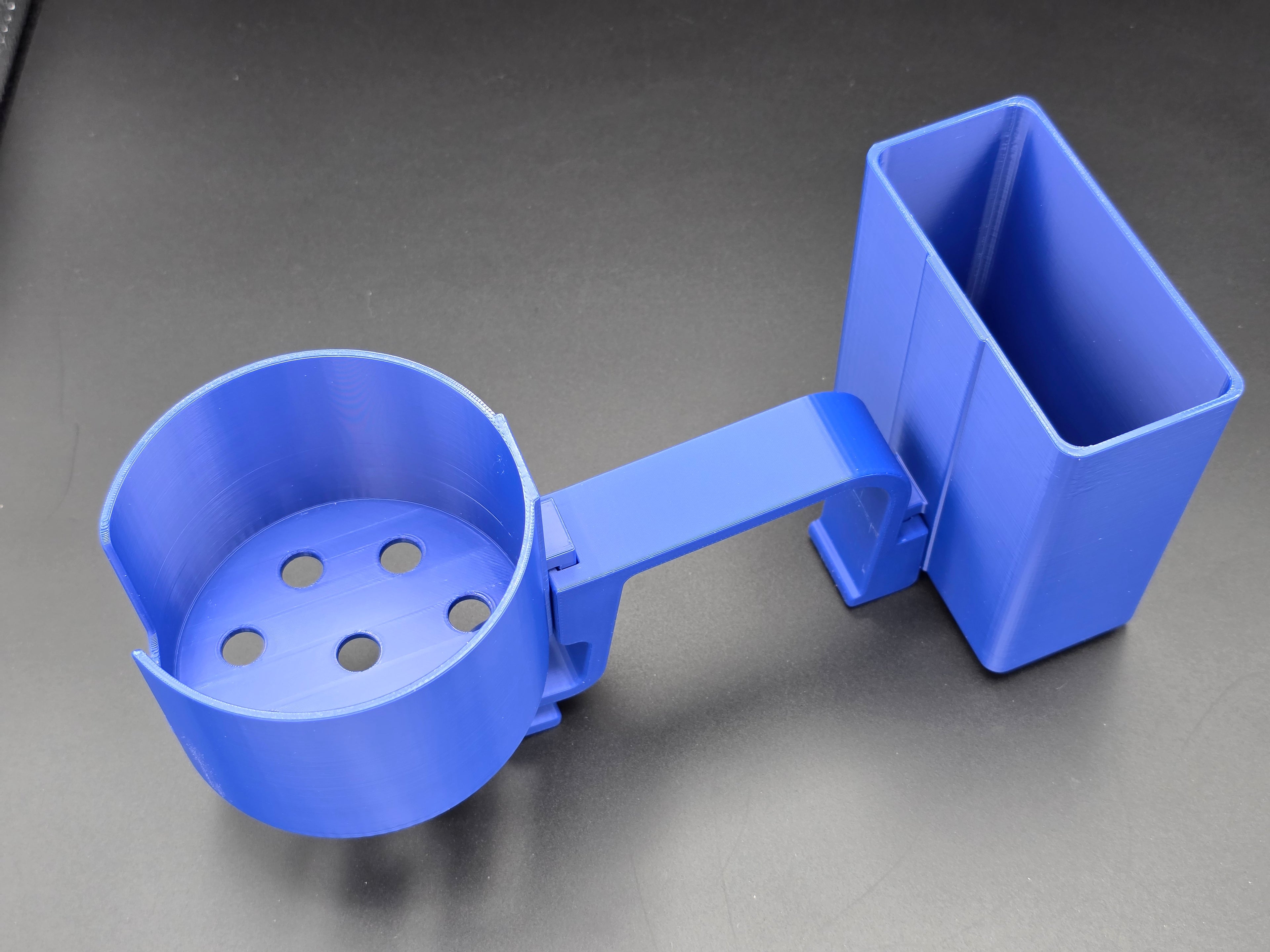 A studio-style shot of a single blue, 3D-printed cup and cell phone holder attachment for a Hastings poly stock tank, isolated against a smooth black background. The cup holder features a deep cylindrical cup with five drainage holes at the bottom and a large side notch for mug handles. The cell phone holder is rectangular with rounded corners. Both holders are connected to a sturdy, integrated L-shaped mounting clip designed to hook over a thick tank rim, showcasing the smooth finish.