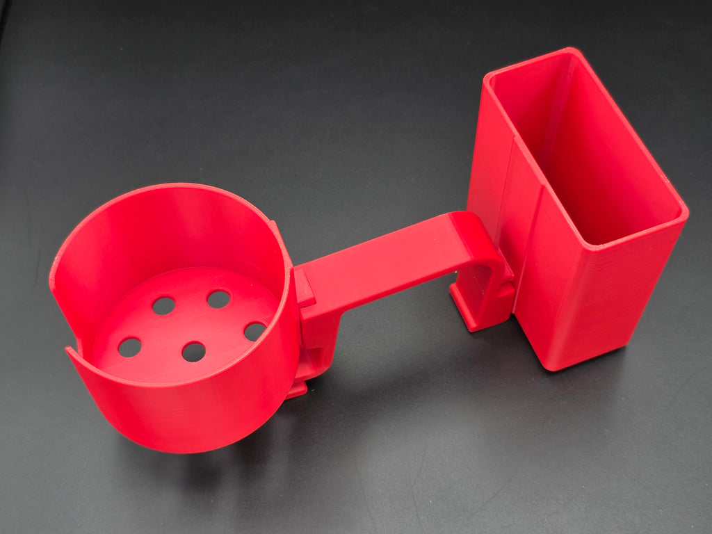 A studio-style shot of a single red, 3D-printed cup and cell phone holder attachment for a Hastings poly stock tank, isolated against a smooth black background. The cup holder features a deep cylindrical cup with five drainage holes at the bottom and a large side notch for mug handles. The cell phone holder is rectangular with rounded corners. Both holders are connected to a sturdy, integrated L-shaped mounting clip designed to hook over a thick tank rim, showcasing the smooth finish.