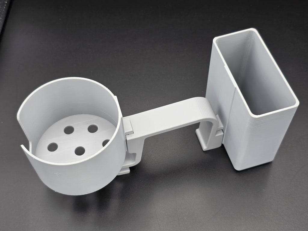 A studio-style shot of a single grey, 3D-printed cup and cell phone holder attachment for a Hastings poly stock tank, isolated against a smooth black background. The cup holder features a deep cylindrical cup with five drainage holes at the bottom and a large side notch for mug handles. The cell phone holder is rectangular with rounded corners. Both holders are connected to a sturdy, integrated L-shaped mounting clip designed to hook over a thick tank rim, showcasing the smooth finish.