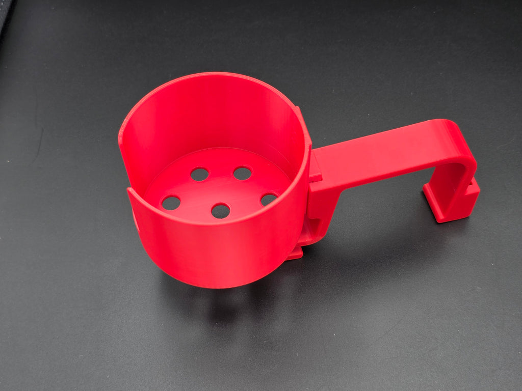 A studio-style shot of a single red, 3D-printed cup holder attachment for a Hastings poly stock tank, isolated against a smooth black background. The holder features a deep cylindrical cup with five drainage holes at the bottom and a large side notch for mug handles. It is connected to a sturdy, integrated L-shaped mounting clip designed to hook over a thick tank rim, showcasing the smooth finish and solid plastic construction of the UV-stable PETG material.