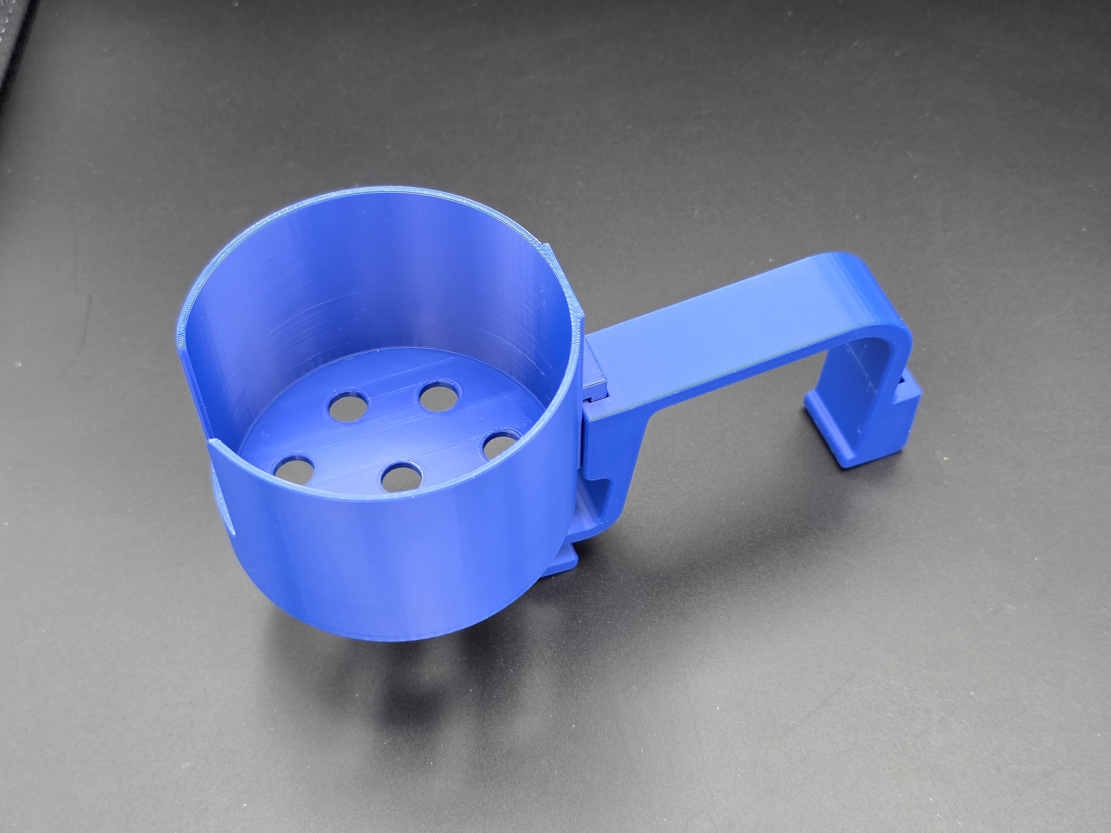 A studio-style shot of a single blue, 3D-printed cup holder attachment for a Hastings poly stock tank, isolated against a smooth black background. The holder features a deep cylindrical cup with five drainage holes at the bottom and a large side notch for mug handles. It is connected to a sturdy, integrated L-shaped mounting clip designed to hook over a thick tank rim, showcasing the smooth finish and solid plastic construction of the UV-stable PETG material.