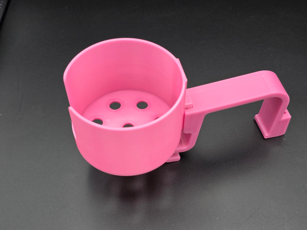 A studio-style shot of a single pink, 3D-printed cup holder attachment for a Hastings poly stock tank, isolated against a smooth black background. The holder features a deep cylindrical cup with five drainage holes at the bottom and a large side notch for mug handles. It is connected to a sturdy, integrated L-shaped mounting clip designed to hook over a thick tank rim, showcasing the smooth finish and solid plastic construction of the UV-stable PETG material.