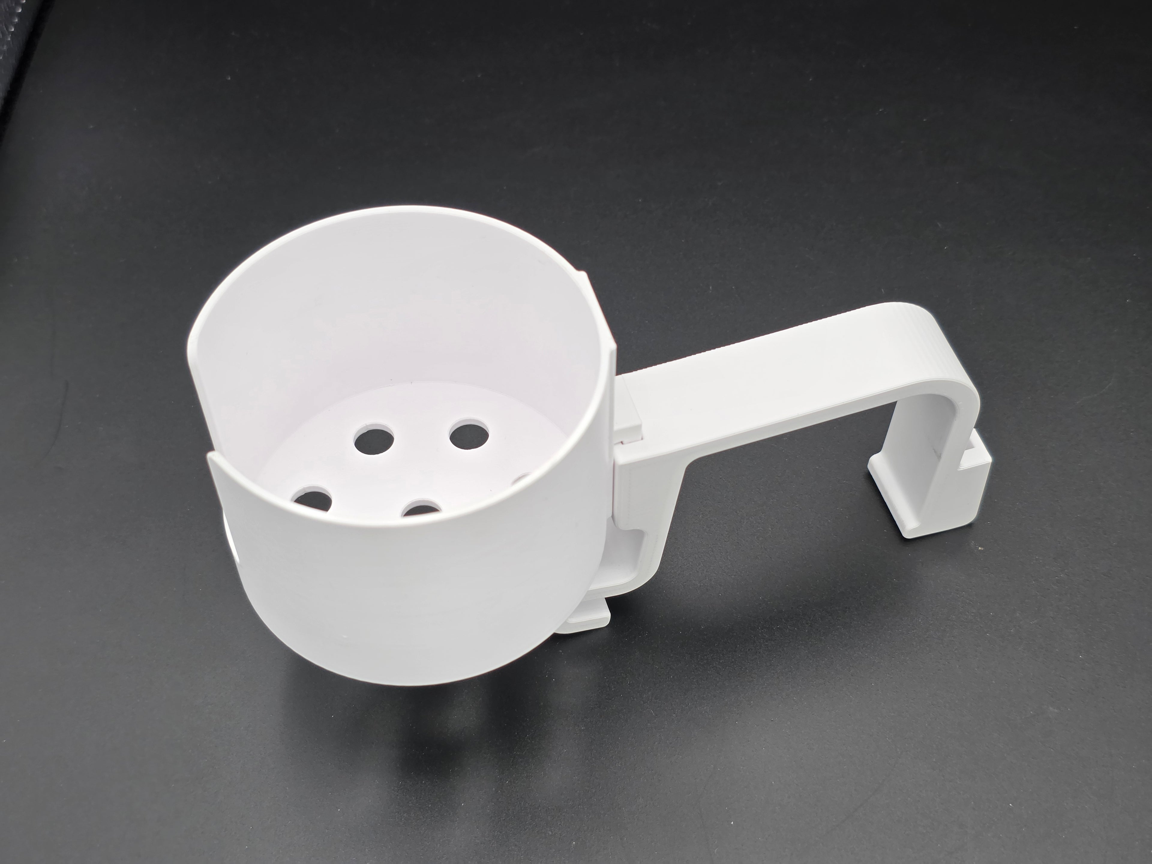 A studio-style shot of a single white, 3D-printed cup holder attachment for a Hastings poly stock tank, isolated against a smooth black background. The holder features a deep cylindrical cup with five drainage holes at the bottom and a large side notch for mug handles. It is connected to a sturdy, integrated L-shaped mounting clip designed to hook over a thick tank rim, showcasing the smooth finish and solid plastic construction of the UV-stable PETG material.