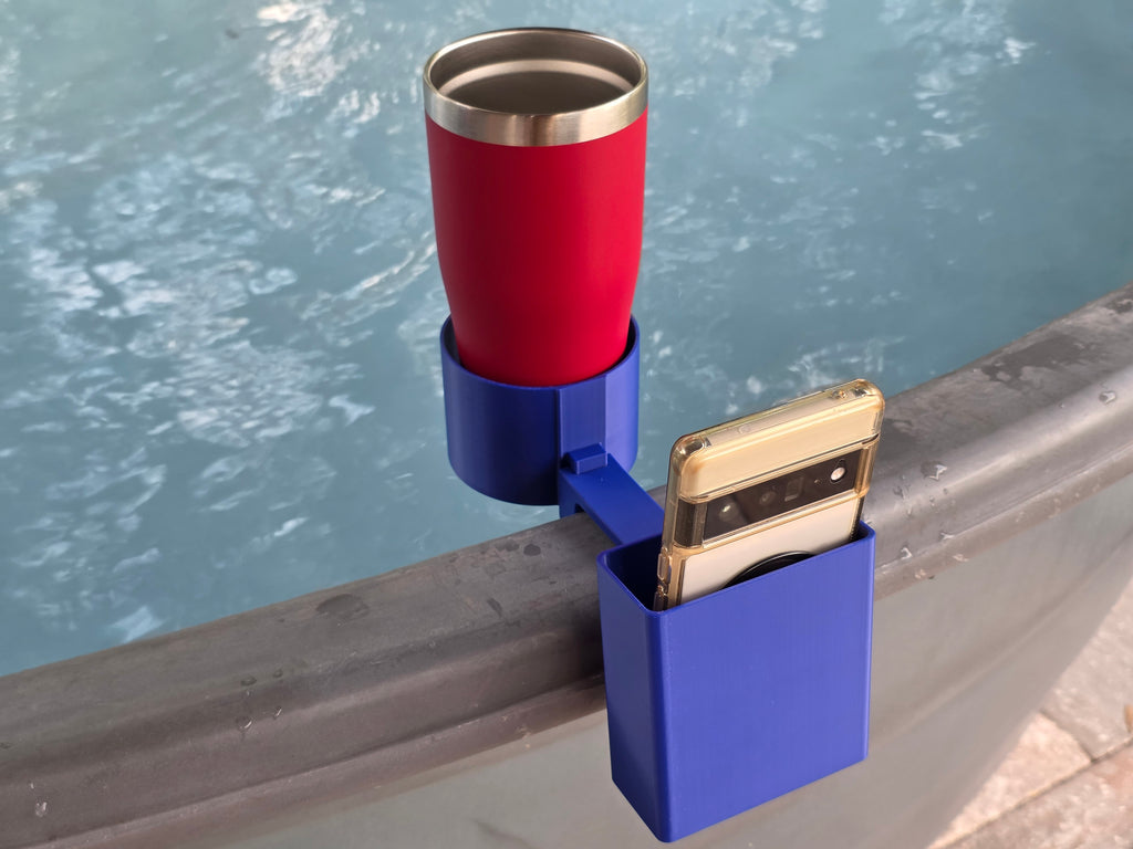 A red insulated tumbler sits in a blue cup holder attached to a stock tank edge. A blue phone holder is next to the tumbler. A white-colored smartphone is in the phone holder. The background is a blue water.