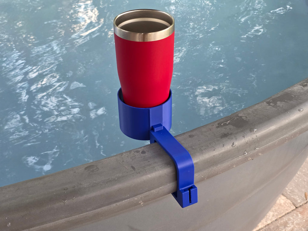 A red insulated tumbler sits in a blue cup holder clamped to the edge of a stock tank. The tumbler has a silver rim and a stainless steel interior. The cup holder is made of plastic and is designed to hold the tumbler securely.