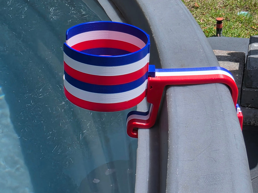 A red, white, and blue striped cup holder, clipped onto the edge of a stock tank. The holder is made of plastic and features a patriotic color scheme.