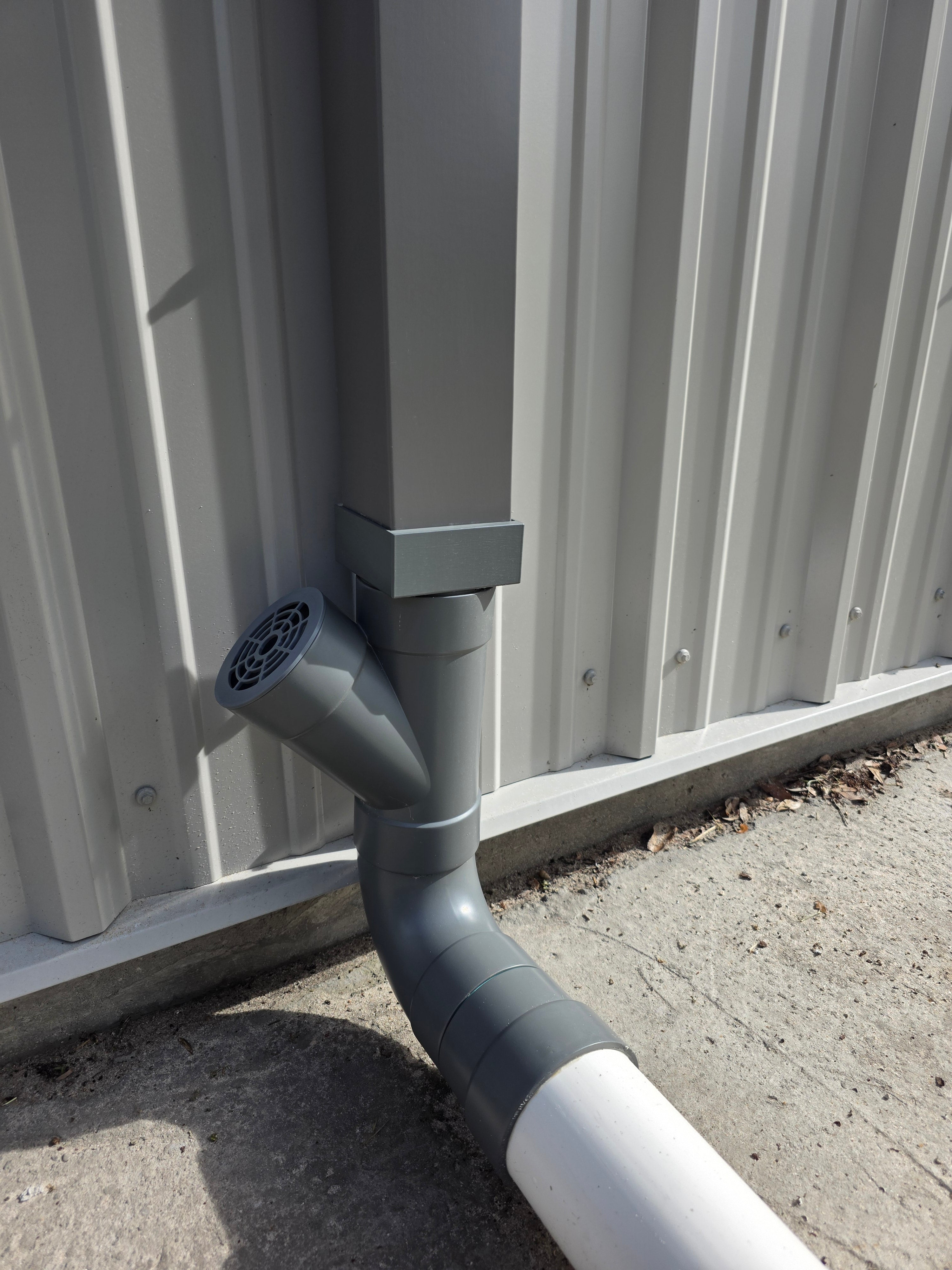 A square grey metal gutter is being adapted to 4" Sewer & Drain (S&D) PVC piping. The 3D Printed adapter and the PVC have been painted tom closely match the grey of the downspout. 