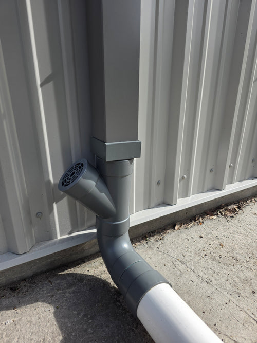 A square grey metal gutter is being adapted to 4" Sewer & Drain (S&D) PVC piping. The 3D Printed adapter and the PVC have been painted tom closely match the grey of the downspout. 