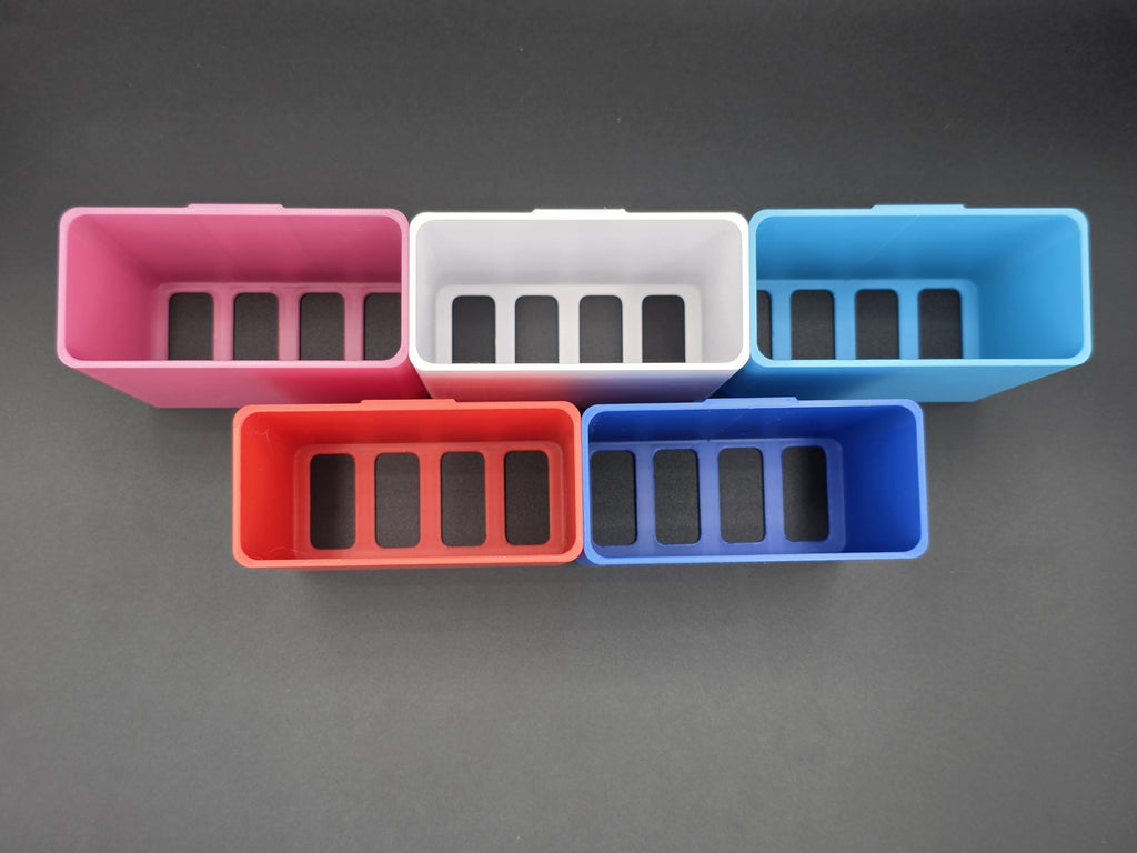 An overhead studio shot of five colorful, 3D-printed cell phone holders arranged on a black background. The holders are shown in pink, white, light blue, red, and blue. 