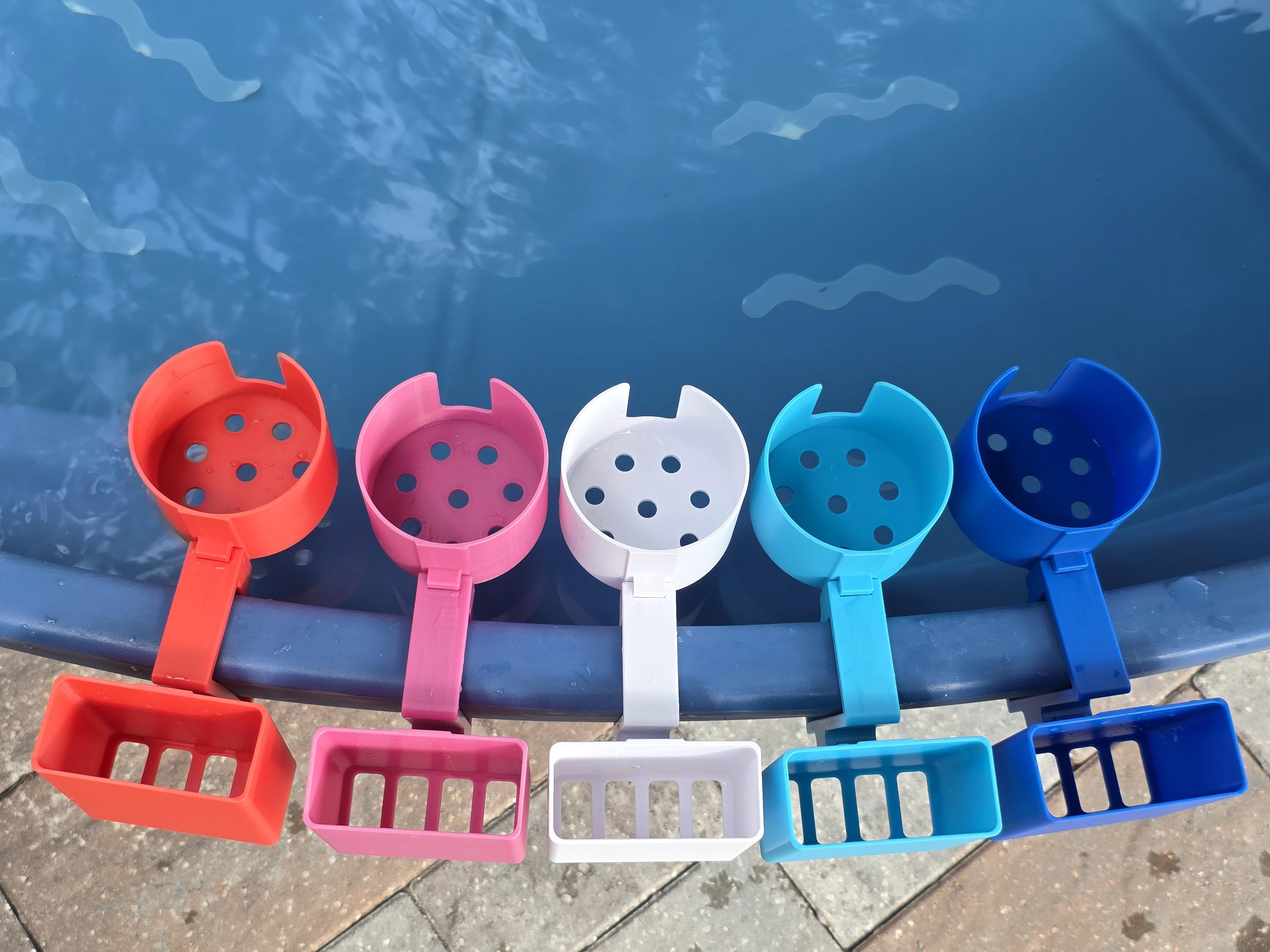 A lineup of vibrant, 3D-printed pool accessories mounted on the blue rim of a stock tank. The shot shows several colorful cup and phone holder attachments in blue, light blue, white, pink, and red, illustrating the modular clip system and the high-quality PETG finish in a backyard poolside setting.