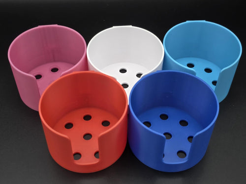 A studio shot of five colorful, 3D-printed cup holders arranged on a black background. The holders are shown in pink, white, light blue, red, and blue, featuring a cutout for mug handles. 