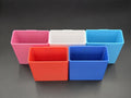 A studio shot of five colorful, 3D-printed cell phone holders arranged on a black background. The holders are shown in pink, white, light blue, red, and blue. 