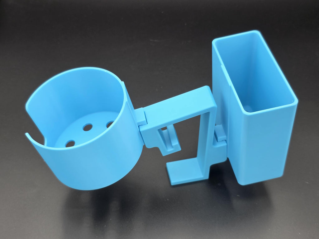 A studio-style shot of a single light blue, 3D-printed cup and cell phone holder attachment for a Tarter poly stock tank, isolated against a smooth black background. The cup holder features a deep cylindrical cup with five drainage holes at the bottom and a large side notch for mug handles. The cell phone holder is rectangular with rounded corners. Both holders are connected to a sturdy, integrated L-shaped mounting clip designed to hook over a thick tank rim, showcasing the smooth finish.