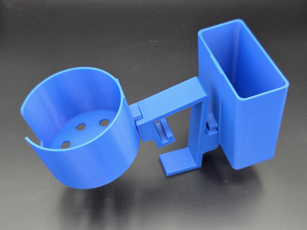 A studio-style shot of a single blue, 3D-printed cup and cell phone holder attachment for a Tarter poly stock tank, isolated against a smooth black background. The cup holder features a deep cylindrical cup with five drainage holes at the bottom and a large side notch for mug handles. The cell phone holder is rectangular with rounded corners. Both holders are connected to a sturdy, integrated L-shaped mounting clip designed to hook over a thick tank rim, showcasing the smooth finish.