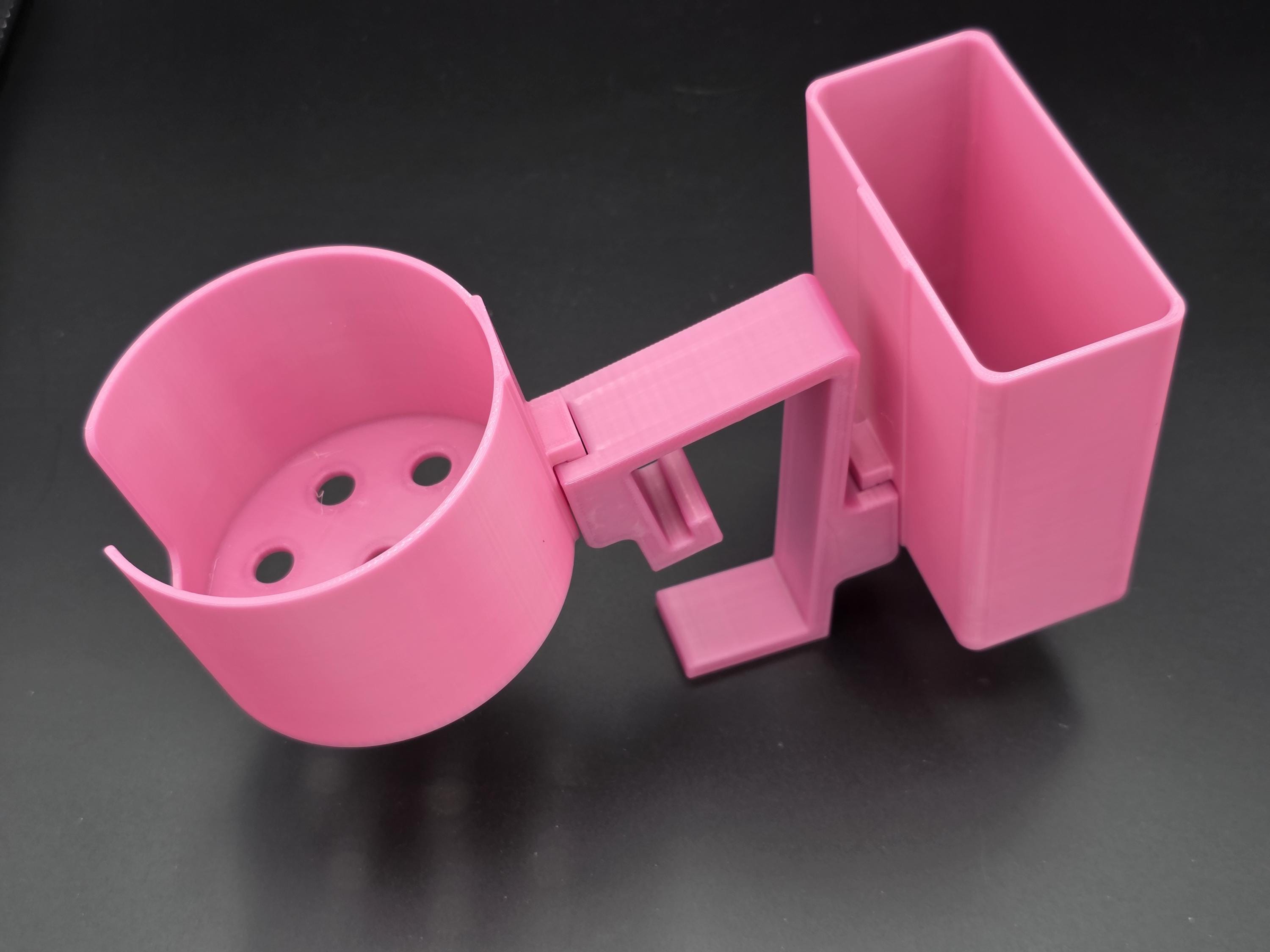 A studio-style shot of a single pink, 3D-printed cup and cell phone holder attachment for a Tarter poly stock tank, isolated against a smooth black background. The cup holder features a deep cylindrical cup with five drainage holes at the bottom and a large side notch for mug handles. The cell phone holder is rectangular with rounded corners. Both holders are connected to a sturdy, integrated L-shaped mounting clip designed to hook over a thick tank rim, showcasing the smooth finish.