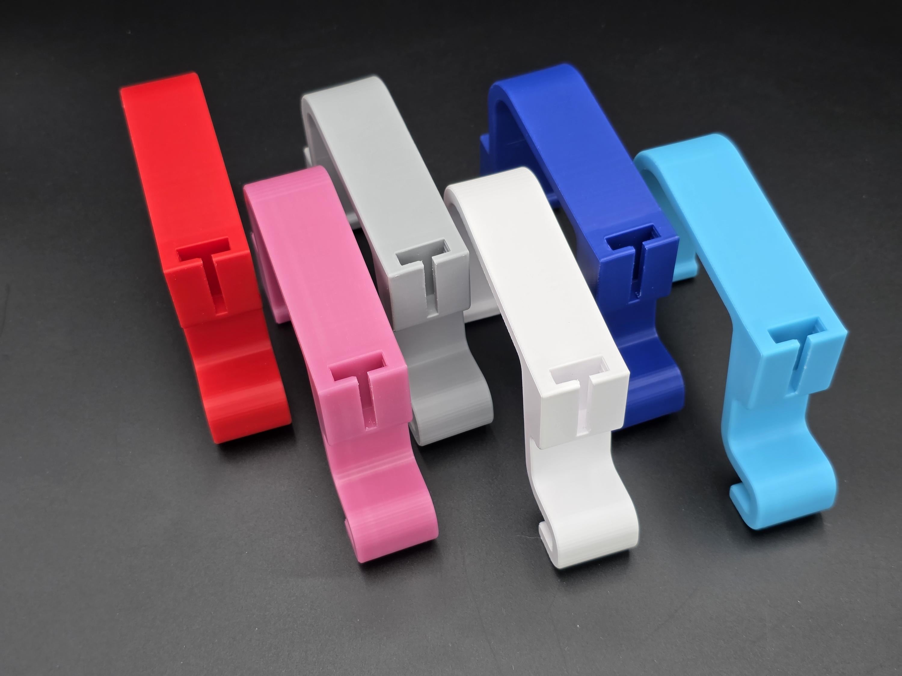 A studio shot of five colorful, 3D-printed Hastings 10ft poly stock tank rim clips arranged on a black background. The clips are shown in pink, white, light blue, red, and blue, featuring a slide in bracket system for accessories. 