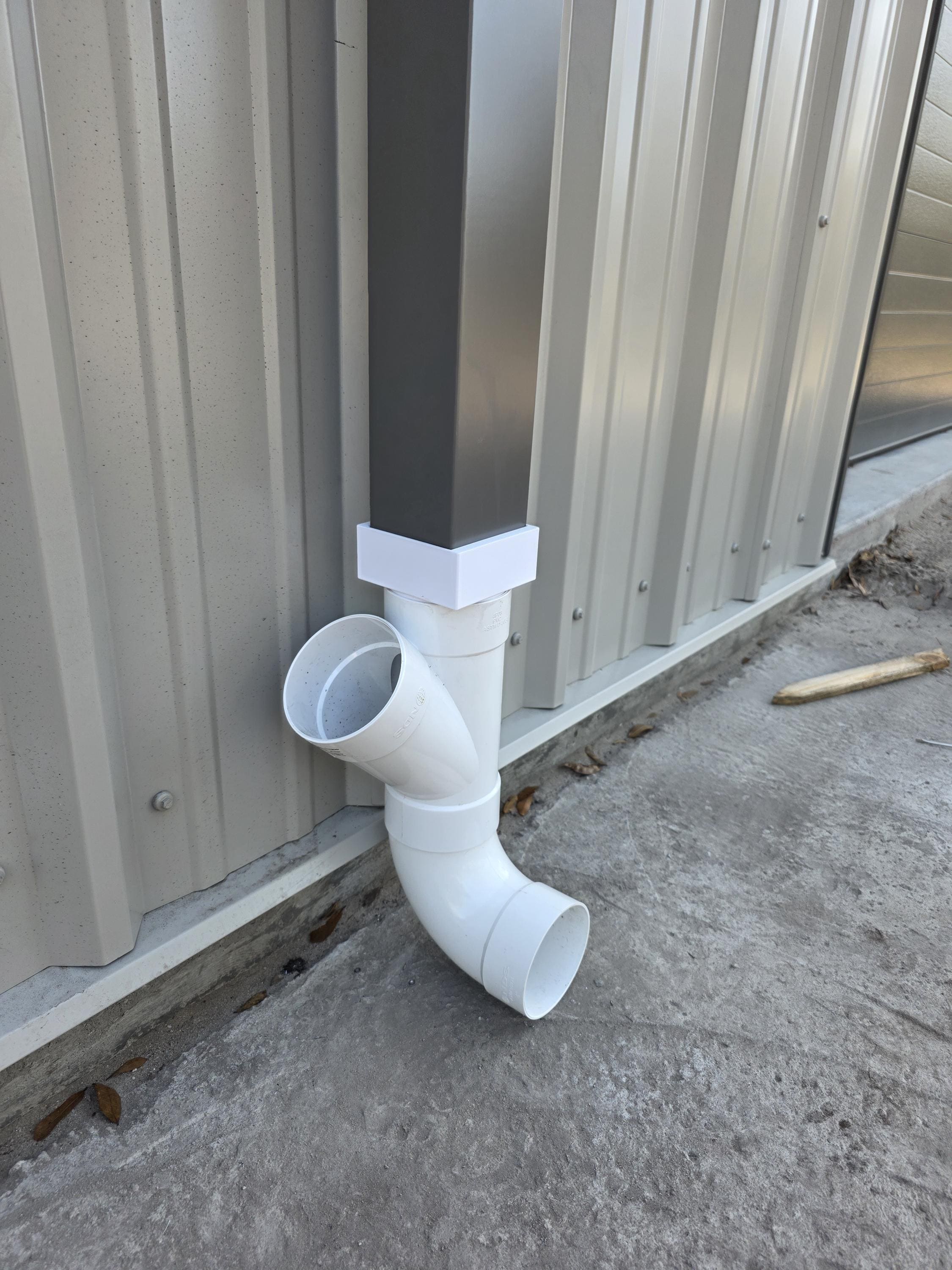 A square grey metal gutter is being adapted to 4" Sewer & Drain (S&D) PVC piping. The 3D Printed adapter and the PVC are shown in their raw un-painted white colors. 