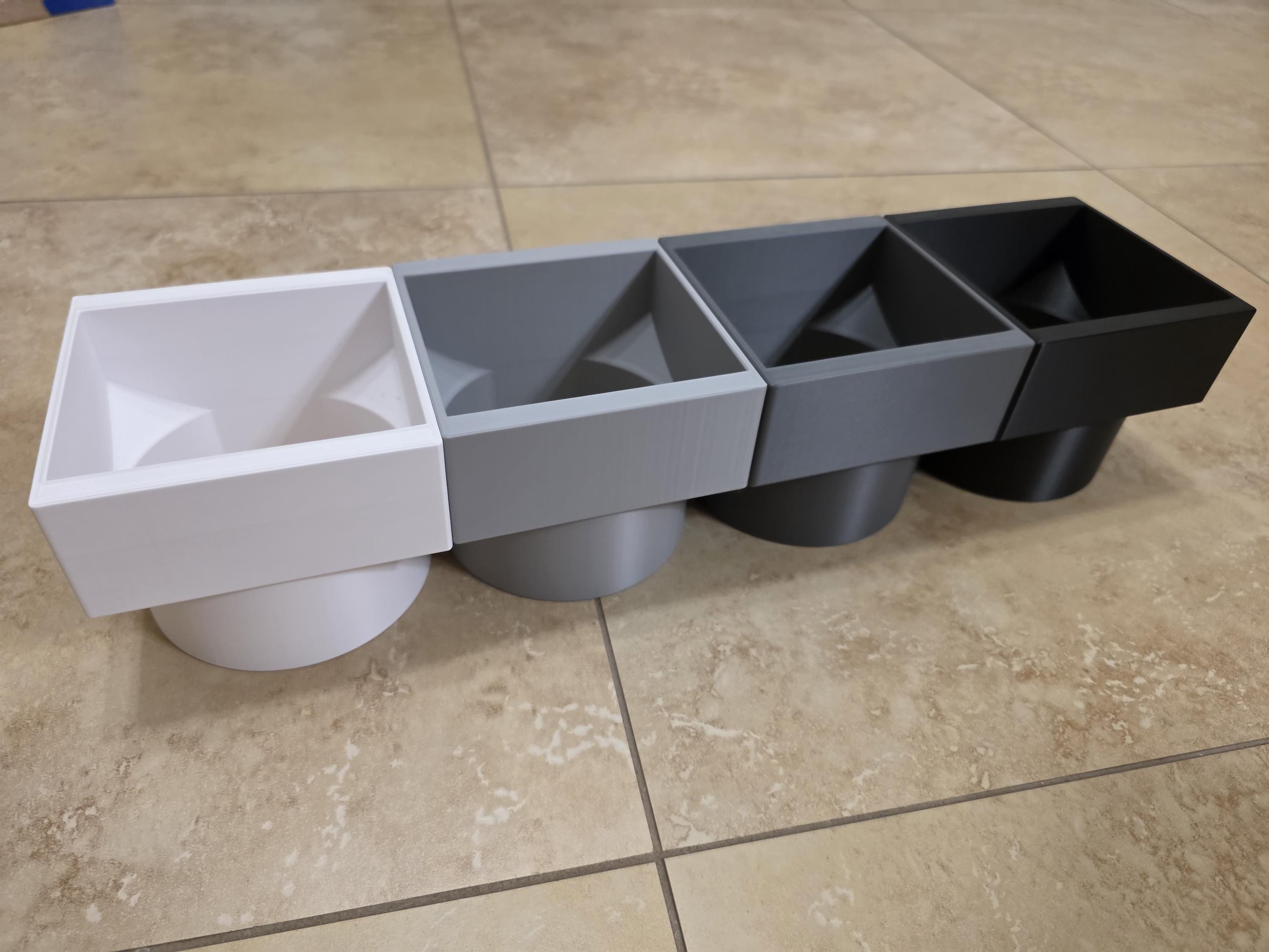 A professional product shot of heavy-duty, 3D-printed downspout adapters made from durable PETG. The adapters feature a clean rectangular top opening designed to slide onto standard gutter downspouts, tapering smoothly into a round bottom outlet for drainage pipes. The precise geometric design and high-quality PETG layer finish are clearly visible against a neutral background. Color options of White, light grey, dark grey, and black are shown. 