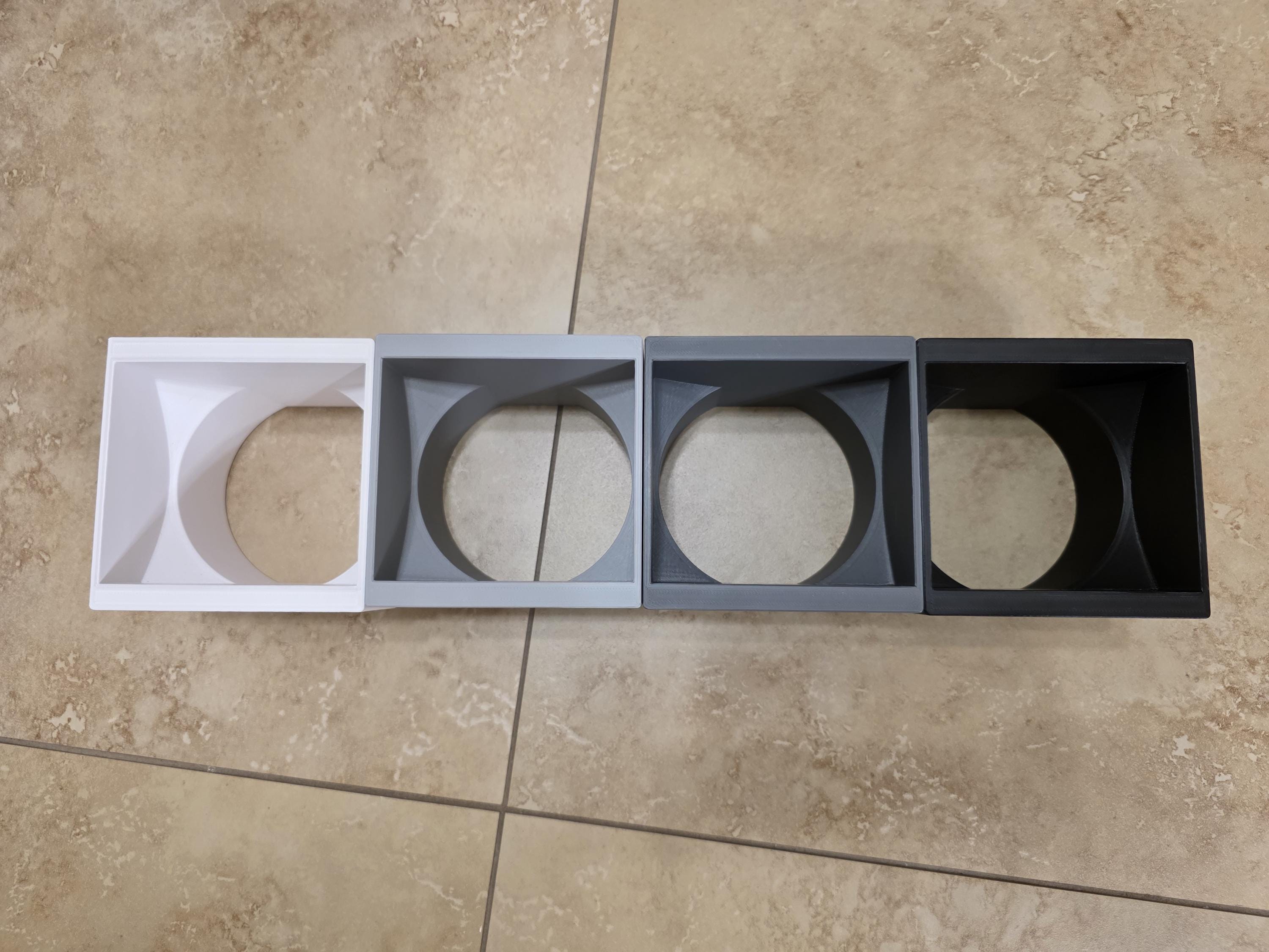 A clean product shot of a white 3D-printed downspout adapter, showing the precise geometric design and smooth PETG plastic finish. The top rectangular opening transitions seamlessly into a round bottom outlet, engineered to cleanly connect home rain gutters to underground drain pipes. Color options of White, light grey, dark grey, and black are shown. 