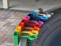 A row of colorful wine glass holders with cell phone caddies in various colors, including green, yellow, orange, red, pink, blue, light blue, white, and grey. Each holder is attached to the rim of a grey stock tank, creating a vibrant and organized display.