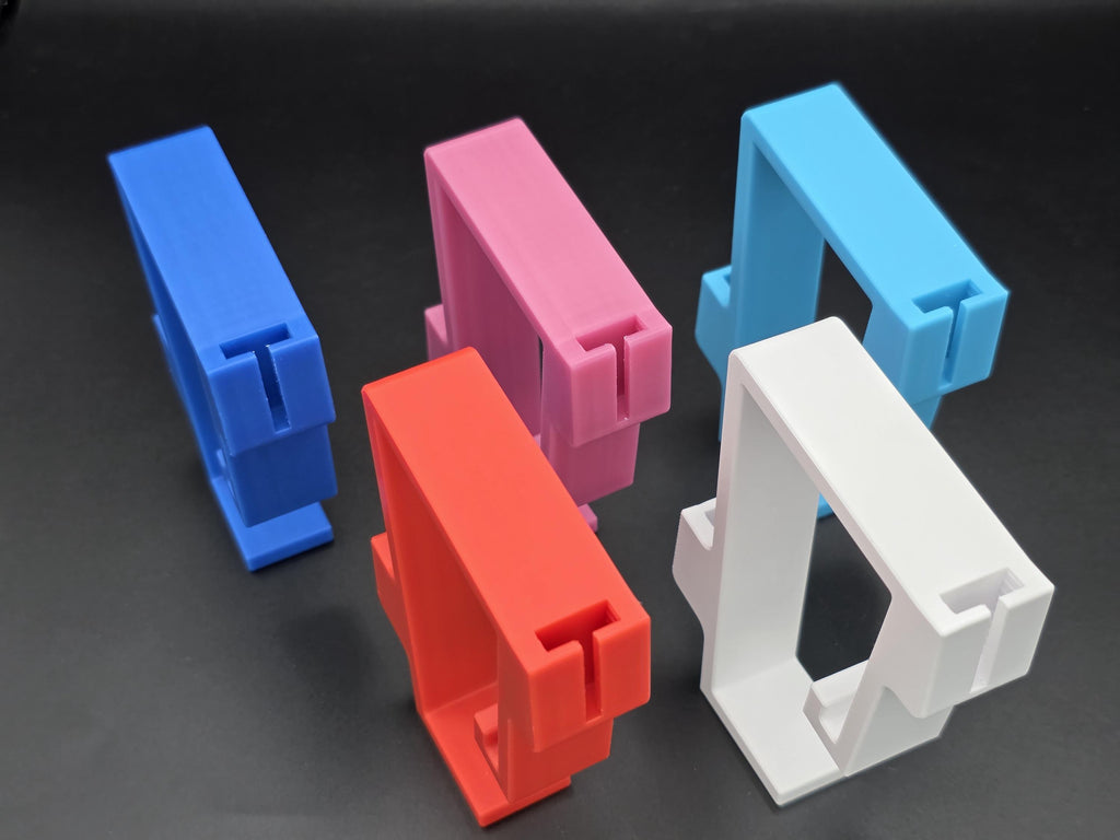 A studio shot of five colorful, 3D-printed Behlen 9ft and 8ft poly stock tank rim clips arranged on a black background. The clips are shown in pink, white, light blue, red, and blue, featuring a slide in bracket system for accessories. 